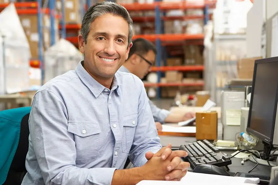Vendor manager sitting at a desk in a warehouse near inventory shelves