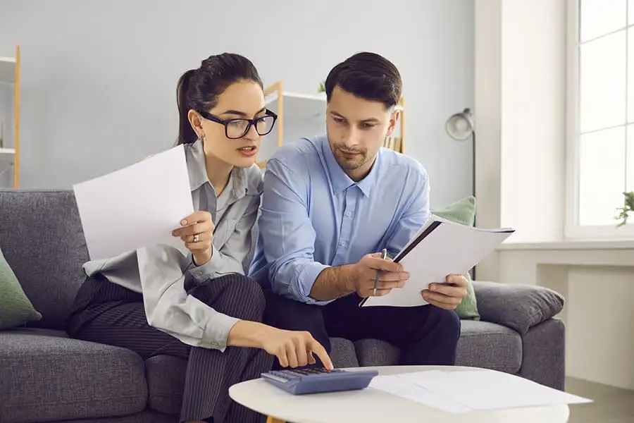 Two colleagues reviewing spend documents and using a calculator on a coffee table