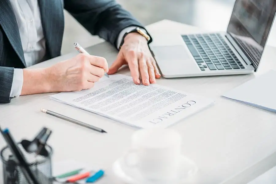 A businessperson signing a printed contract beside an open laptop