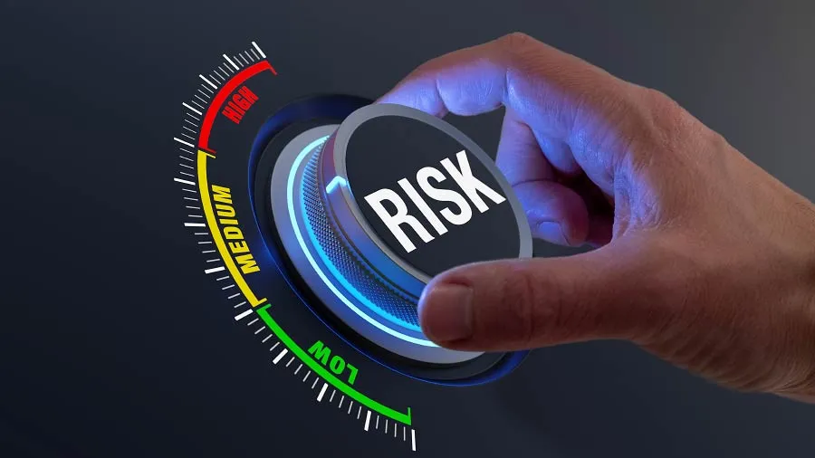 Close-up of a hand turning a dial labeled RISK across a LOW, MEDIUM, HIGH gauge against a dark background.