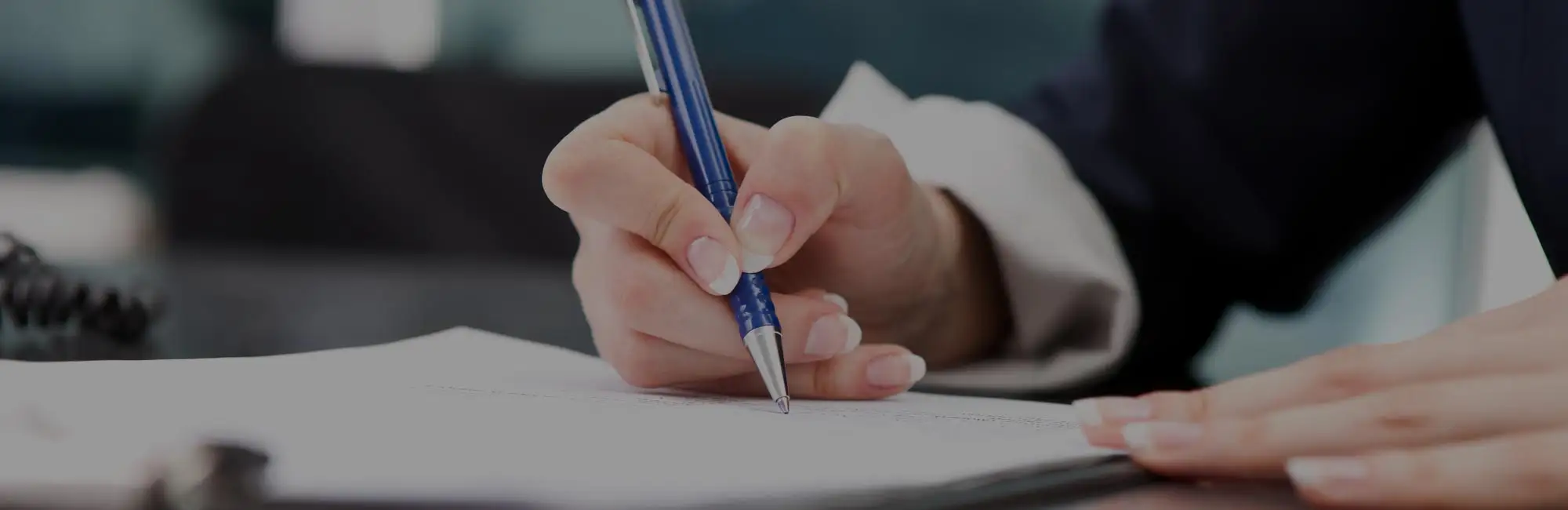 Close-up of a hand signing a printed contract with a pen