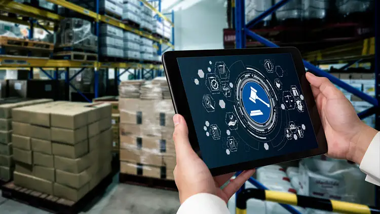 A warehouse worker holds a tablet showing a compliance and legal icon over rows of stacked pallets