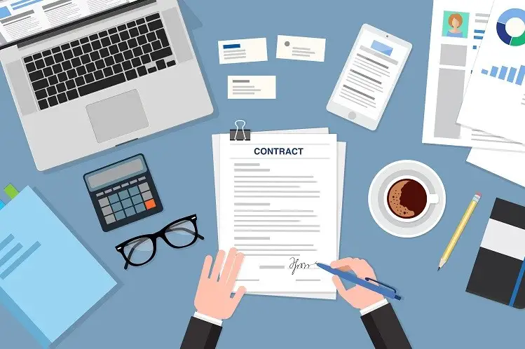 A businessperson signing a printed contract at a desk surrounded by a laptop, calculator, phone and coffee