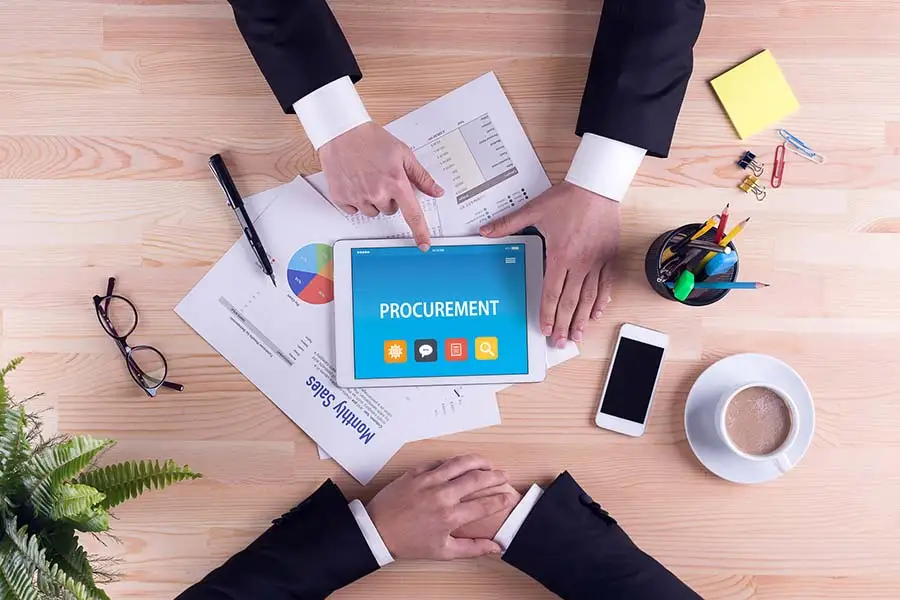 Overhead view of a desk with a tablet showing a procurement app and spend charts