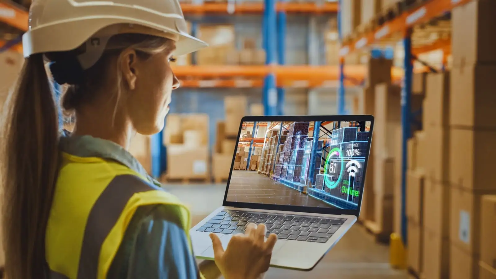 Warehouse worker in a hard hat reviewing AI-powered inventory analytics on a laptop
